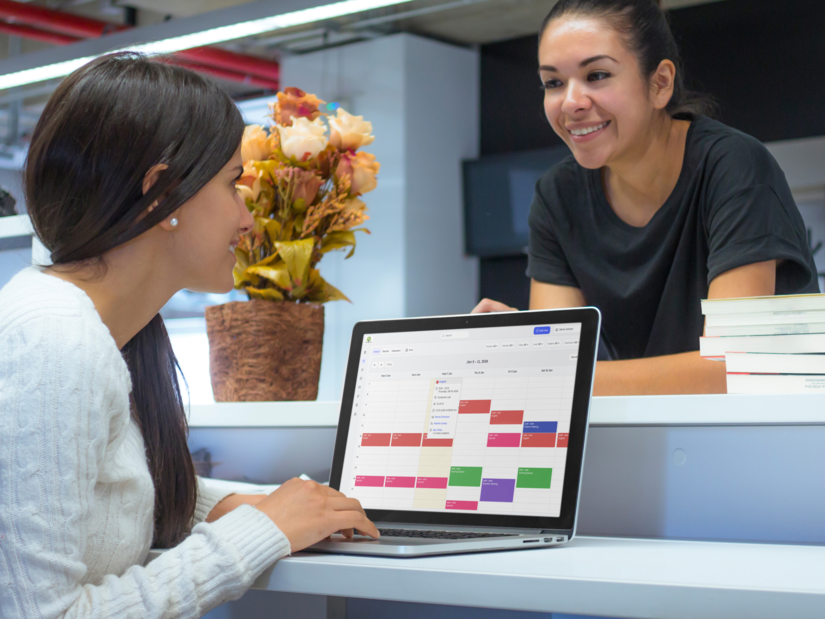 School administrator using a laptop to manage teacher schedules in a classroom.